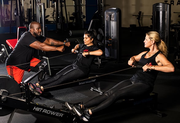 Trainer with two women working out on rowing machine